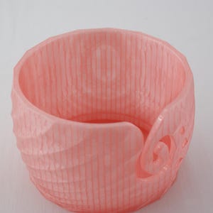 Peut inclure: Un bol à laine rose avec une surface texturée et un motif en spirale décoratif. Le bol est conçu pour contenir de la laine pour le tricot ou le crochet.