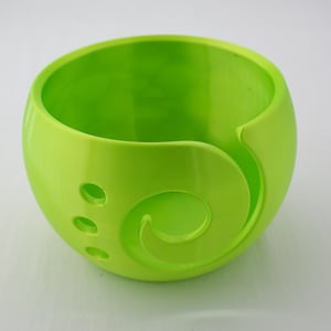 Può includere: Ciotola per filato verde brillante con forma arrotondata e un design a spirale sul lato. La ciotola ha tre piccoli fori e una fessura curva per tenere il filato durante la lavorazione a maglia o all'uncinetto. Superficie liscia e lucida.