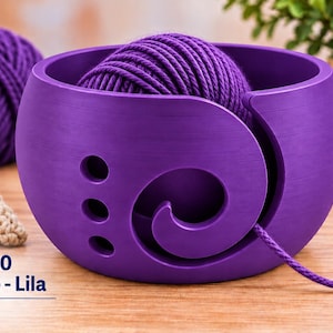 Può includere: Una ciotola per lana viola rotonda con un intaglio a spirale e tre fori circolari sul lato. Un gomitolo di lana viola si trova all'interno della ciotola con un filo che passa attraverso la spirale. Il testo SD-010 Purple - Lila Amethyst è presente.