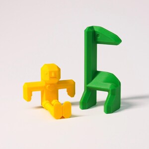 May include: A yellow 3D printed toy figure of a person sitting on a green 3D printed toy chair shaped like a giraffe.