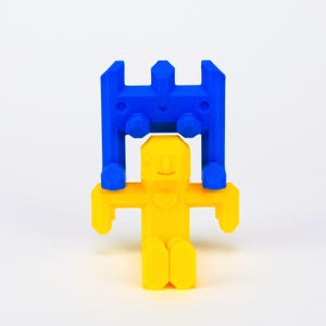 May include: A yellow toy figure with a heart on its chest is being held up by a blue toy structure.