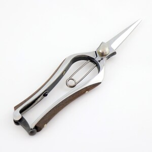 K&ouml;nnte beinhalten: Eine silberne Gartenschere mit einem Holzgriff. Die Schere hat einen Federmechanismus und eine Sicherheitsverriegelung.