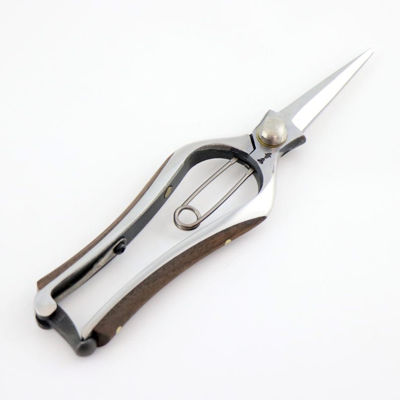 K&ouml;nnte beinhalten: Eine silberne Gartenschere mit einem Holzgriff. Die Schere hat einen Federmechanismus und eine Sicherheitsverriegelung.