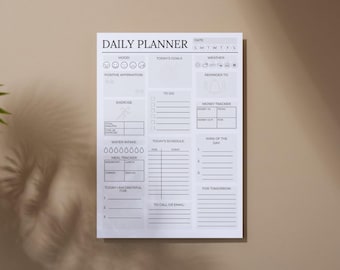 May include: A white daily planner with sections for mood, goals, to-do lists, and a money tracker. The planner includes sections for exercise, water intake, and a meal tracker. The top of the planner reads "DAILY PLANNER".