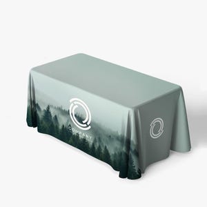 May include: A rectangular tablecloth with a forest scene printed on it. The design features a misty forest with evergreen trees. The tablecloth has a company logo in white. The color of the tablecloth is a light green.