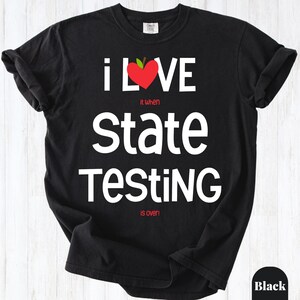 May include: A black short-sleeved t-shirt featuring the white text "I LOVE" with a red heart-shaped apple replacing the letter "O". Below this, the text reads "it when" in red, "STATE TESTING" in white, and "is over!" in red lettering.