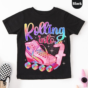 May include: A black short-sleeve t-shirt featuring a graphic of a pink roller skate with rainbow laces and a heart detail. The text reads Rolling into 7, with the number 7 topped by a small crown. The design includes colorful galaxy patterns.