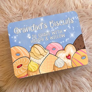 May include: A rectangular biscuit tin with a light blue background, featuring the words "Grandad's Biscuits" in white script. The tin is decorated with illustrations of biscuits and donuts. The text "TO SHARE WITH HARRY & WILLOW" is also present.