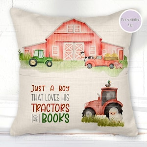 May include: A beige cushion featuring a watercolour farm scene. A red barn, green tractor, red truck, and a red tractor with a duck are shown. The text reads, "Just a boy that loves his tractors and books."