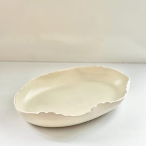 May include: A white ceramic oval serving dish with a scalloped edge.