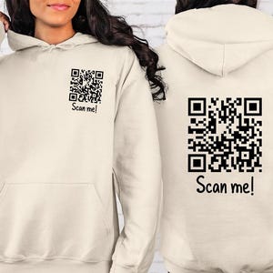 May include: A cream-coloured hoodie with a black QR code and the text "Scan me!" on the front and back.