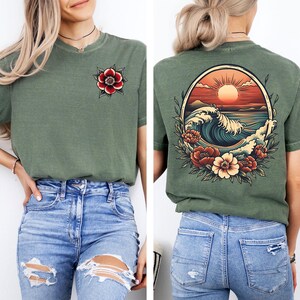 May include: A green t-shirt with a floral design on the left side and a wave design with a sunset on the back. The shirt is being modeled by a person wearing blue jeans.