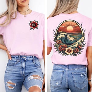 May include: Pink t-shirt with a floral design on the left side and a vintage-style illustration of a wave, sunset, and flowers on the back.