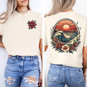 May include: A white t-shirt with a red flower on the front and a vintage-style illustration of a wave crashing in the ocean with a sunset behind it on the back.