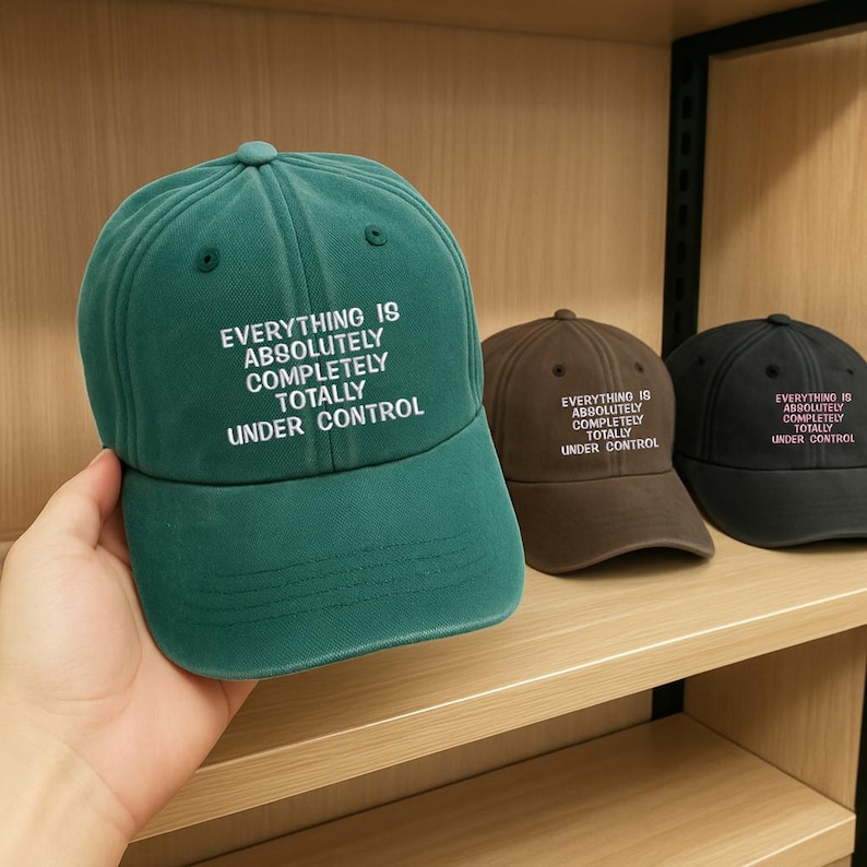 May include: A green baseball cap with the text "EVERYTHING IS ABSOLUTELY COMPLETELY TOTALLY UNDER CONTROL" in white. The image also shows a brown and a black cap with the same text.