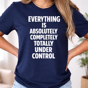 May include: A navy blue t-shirt featuring the white text "EVERYTHING IS ABSOLUTELY COMPLETELY TOTALLY UNDER CONTROL". The text is stacked. The shirt has a crew neck and short sleeves.