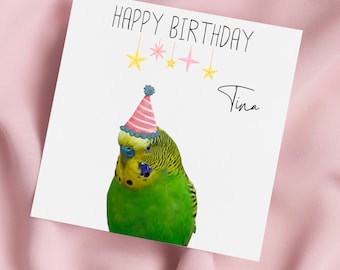 Pode incluir: Cartão de feliz aniversário com um periquito verde e amarelo usando um chapéu de festa rosa e vermelho. O cartão tem o texto "Feliz aniversário" e "Tina" escrito nele.