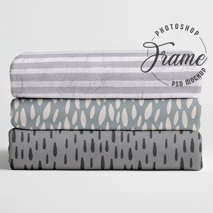 May include: Three folded fabric items are stacked, each with a unique pattern. The top item features grey and white stripes. The middle item has a teal background with white ovals. The bottom item has a grey background with black teardrop shapes. The image includes the text "Photoshop Frame PSD Mockup".