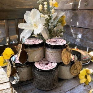 Peut inclure: Six pots en verre avec des couvercles noirs et des &eacute;tiquettes roses contenant des gommages au sucre. Les &eacute;tiquettes portent les mentions "Simply Sweet" et "Sugar Scrub". Les pots sont dispos&eacute;s en forme de pyramide sur une surface en bois.