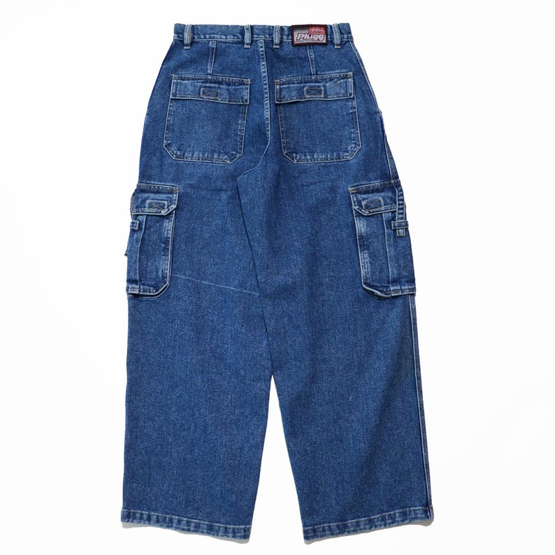 May include: Blue denim cargo pants with multiple pockets, including two large side pockets and two back pockets. The pants have a wide leg design and a "Rhino" label on the back. The denim is a medium wash.