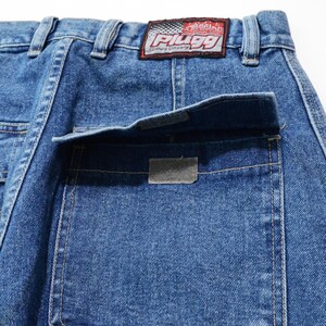 May include: Close-up of blue denim jeans with a back pocket and a rectangular patch. The jeans have a "PLUGG Clothing Company" label on the back. The denim is a medium wash with visible stitching.