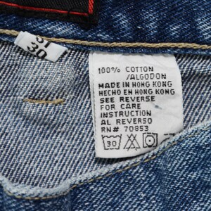 May include: Close-up of blue denim jeans with a white tag. The tag reads "100% COTTON / ALGODON MADE IN HONG KONG" and includes care instructions. A smaller tag shows the size "30".