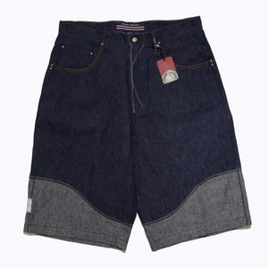 May include: Dark wash denim shorts with a gray panel design at the hem. The shorts have a classic five-pocket design with a button and zipper closure. A red tag hangs from the front. The shorts are a casual style.