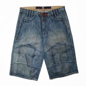 May include: Blue denim shorts with a faded wash and a brown leather belt loop. The shorts have a unique patchwork design on the front and back, with decorative stitching along the pockets and seams. The shorts have a button closure and a zipper fly.