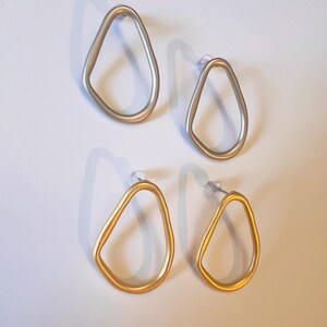 May include: Four pairs of open-frame earrings. Two pairs are silver-toned, and two are gold-toned. Each earring has a teardrop shape with a post backing. The earrings are displayed on a white surface. The earrings are suitable for pierced ears.