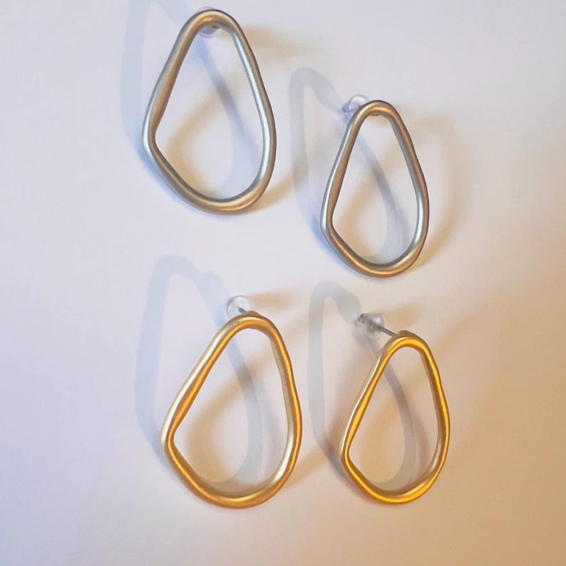 May include: Four pairs of open-frame earrings. Two pairs are silver-toned, and two are gold-toned. Each earring has a teardrop shape with a post backing. The earrings are displayed on a white surface. The earrings are suitable for pierced ears.