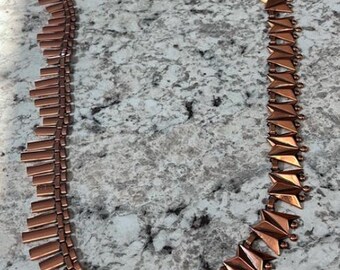 May include: A copper necklace with a geometric design. The necklace is made of two different styles of links, one with rectangular links and the other with triangular links.