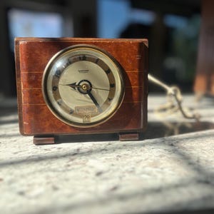 May include: A vintage wooden clock with a round, white face and gold hands. The clock face has the words "WEDNESDAY" and "29" printed on it. The clock is made by the "HAMMOND" company.