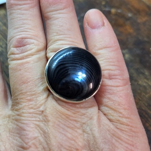 May include: A silver ring with a black and gray round gemstone