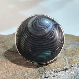 Puede incluir: Un anillo de plata con una piedra preciosa negra y verde. La piedra preciosa tiene un patr&oacute;n de remolino.