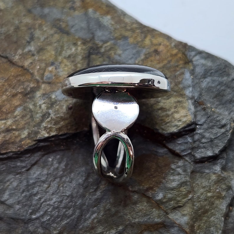 Puede incluir: Un anillo de plata con una piedra ovalada negra. El anillo tiene una banda &uacute;nica y retorcida.