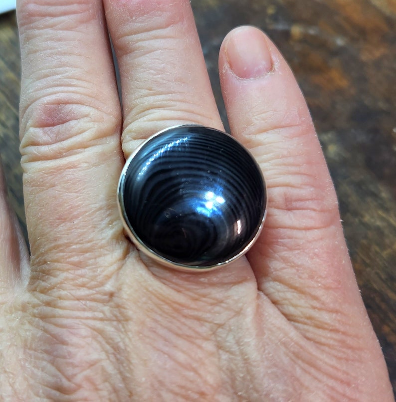 May include: A silver ring with a black and gray round gemstone