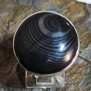 Puede incluir: Un anillo de plata con una piedra preciosa negra y gris. La piedra preciosa tiene un patr&oacute;n de remolino.