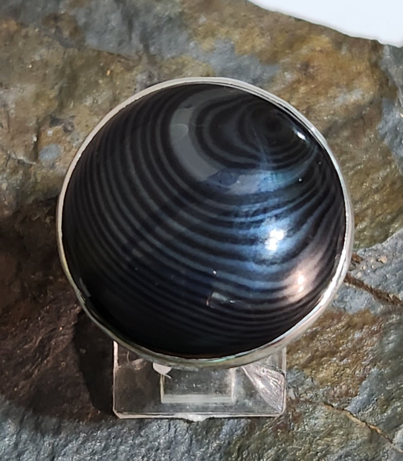 Puede incluir: Un anillo de plata con una piedra preciosa negra y gris. La piedra preciosa tiene un patr&oacute;n de remolino.