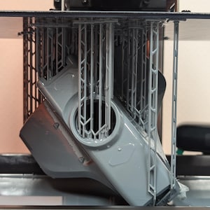 Könnte beinhalten: Ein 3D-gedrucktes Objekt aus grauem Kunststoff wird auf einem 3D-Drucker gedruckt. Das Objekt ist durch eine Reihe von Stützstrukturen in der Luft gehalten.