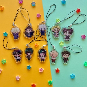 May include: A collection of anime-style character charms with black lanyards. The charms feature various characters in different outfits. Scattered around are colorful star-shaped decorations on a yellow and teal background.