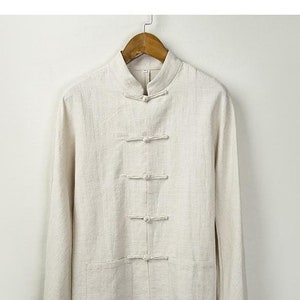 May include: A cream linen shirt with a mandarin collar and five button fastenings. The shirt has long sleeves and two pockets.