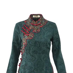 Puede incluir: Una chaqueta de color azul verdoso con cuello mandarín, ribetes florales y botones rojos. La chaqueta tiene un estampado floral y un nudo decorativo en la parte delantera.