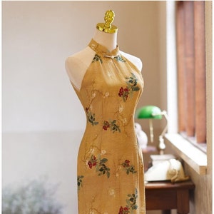 May include: A yellow halter dress with a floral print. The dress has a mandarin collar and a fitted silhouette.