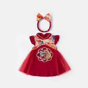 Könnte beinhalten: Rotes Babykleid mit passendem Stirnband. Das Kleid hat ein florales Design auf dem Oberteil und ein goldgesticktes Emblem auf der Vorderseite. Das Kleid hat einen Tüllrock und Rüschenärmel.