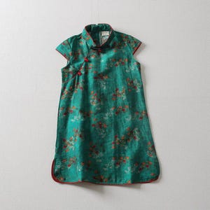 Puede incluir: Vestido verde sin mangas con cuello mandarín y ribete rojo. El vestido presenta un estampado floral en tonos rojos, naranjas y blancos. Tiene cierre de botón y un corte holgado. Mide unos 90 cm de largo.