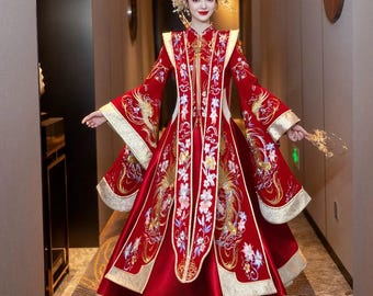 May include: A woman wearing a traditional Chinese red dress with gold embroidery and a long train. The dress features a high collar and long sleeves. The woman is standing in a hallway with a gold and white patterned carpet.