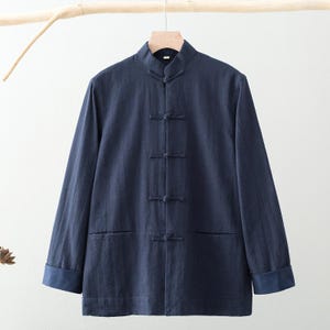 May include: A navy blue long-sleeved jacket with a mandarin collar and frog closures. The jacket has two front pockets and dark blue cuffs. The garment is hanging on a wooden hanger against a white background.