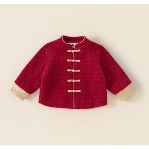 May include: A red jacket with a mandarin collar and gold frog closures. The sleeves have gold trim at the cuffs. The jacket is a traditional style, likely for a child.