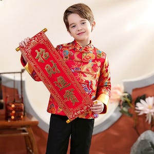 May include: A young person in a red and gold traditional Chinese jacket with a dragon design, holding a red scroll with gold lettering. The jacket has gold trim and buttons. The scroll has gold accents.