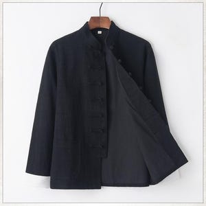 Op de afbeelding: Een zwart linnen jack met een mandarijnsluiting en een rij knopen aan de voorkant. Het jack heeft een zak aan de linkerkant en is open, waardoor een zwarte voering zichtbaar is.